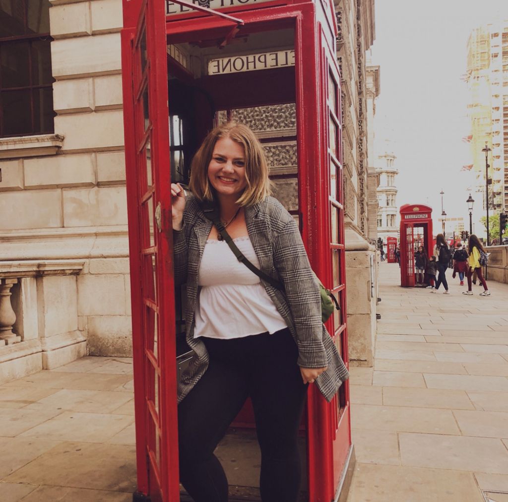 Girl smiling at camera inside a red British Telephone box. 