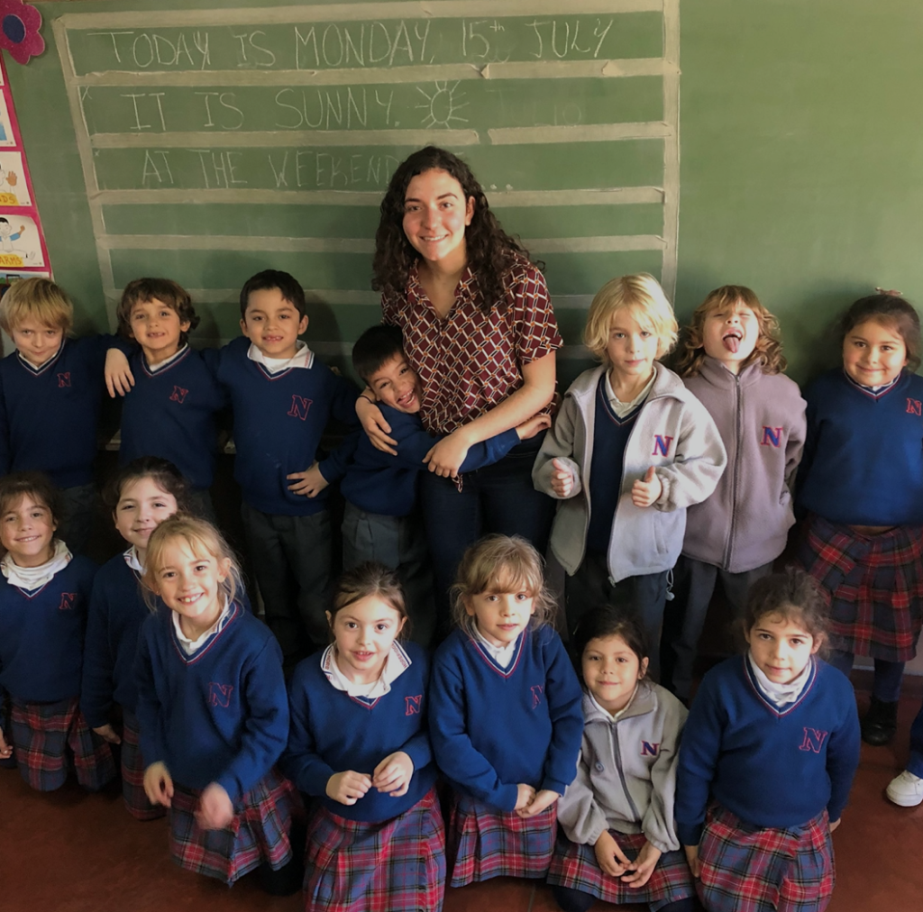 Woman smiling at camera with group of small children in school uniforms. 