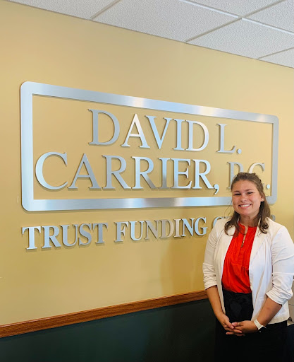 woman in white cardigan and red shirt smiling at camera next to law firm sign